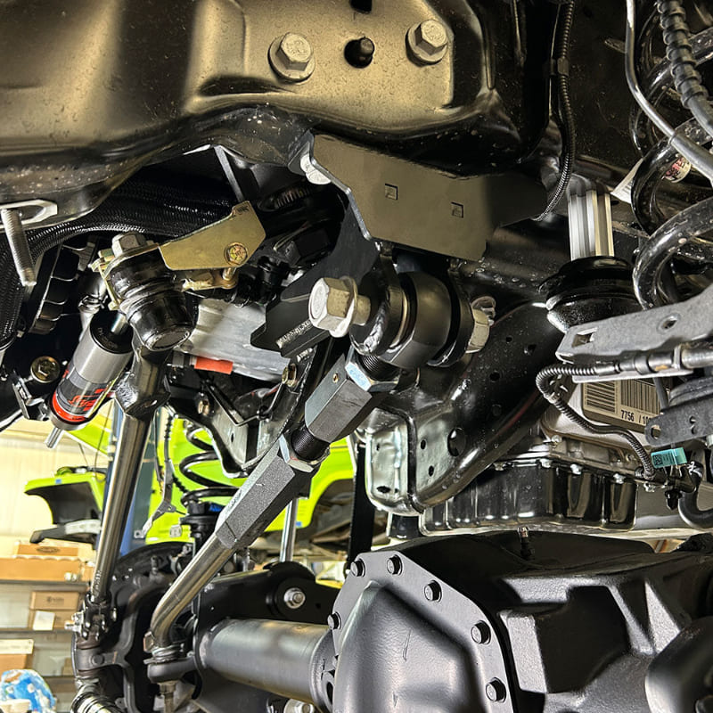 Undercarriage view of a vehicle showing the front suspension of an SB Suspension Kit and steering system components.