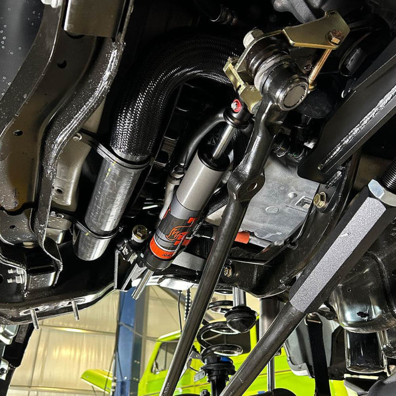 Undercarriage view of a vehicle showing the front suspension of an SB Suspension Kit and steering system components.