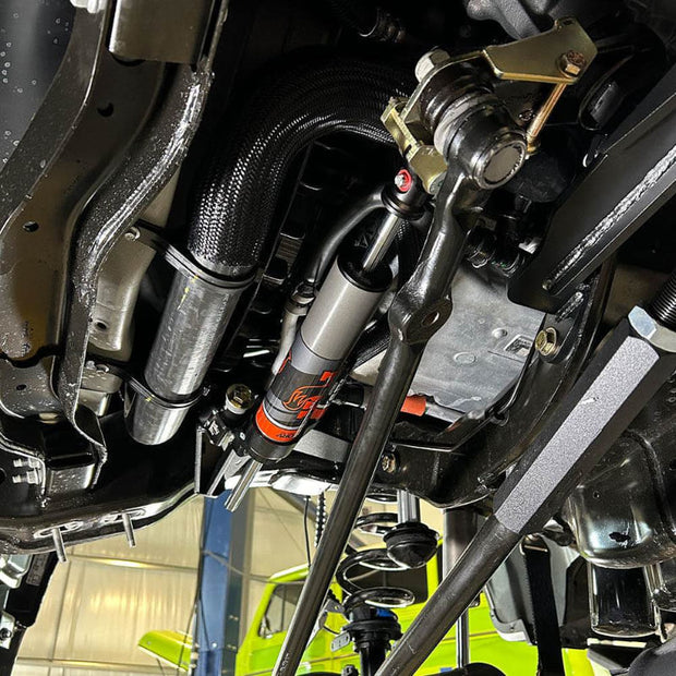 Undercarriage view of a vehicle showing the front suspension of an SB Suspension Kit and steering system components.