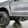 A silver 2023+ Ford power stroke truck with a 2.5 inch lift kit, showcasing the raised front and the new aftermarket wheels and tires.