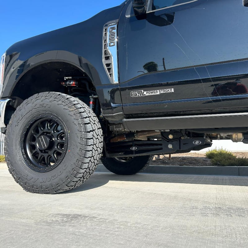 A black 2023+ Ford F250/F350 truck with a 2.5 inch lift kit, showcasing the raised front and the new aftermarket wheels and tires.
