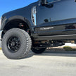 A black 2023+ Ford F250/F350 truck with a 2.5 inch lift kit, showcasing the raised front and the new aftermarket wheels and tires.