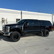 A black 2023+ Ford F250/F350 truck with a 2.5 inch lift kit, showcasing the raised front and the new aftermarket wheels and tires.
