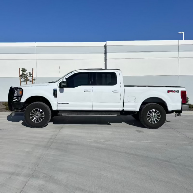A white 2017-2022 Ford F250/F350 truck with leveling kit, showing the front side profile on a clear day.