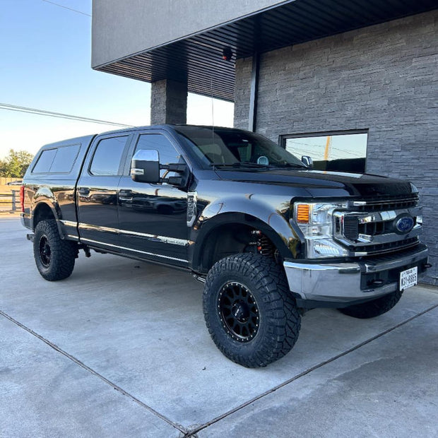 A black lifted truck parked outside a building, showcasing off-road tires and a front-end lift kit.