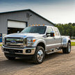 A silver Ford F450 truck parked in front of a building with a workshop or garage interior.