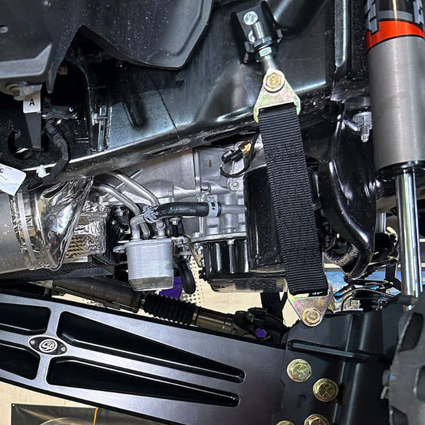 A black limit strap kit installed on a vehicle, showing the strap attached to the frame underneath the car.