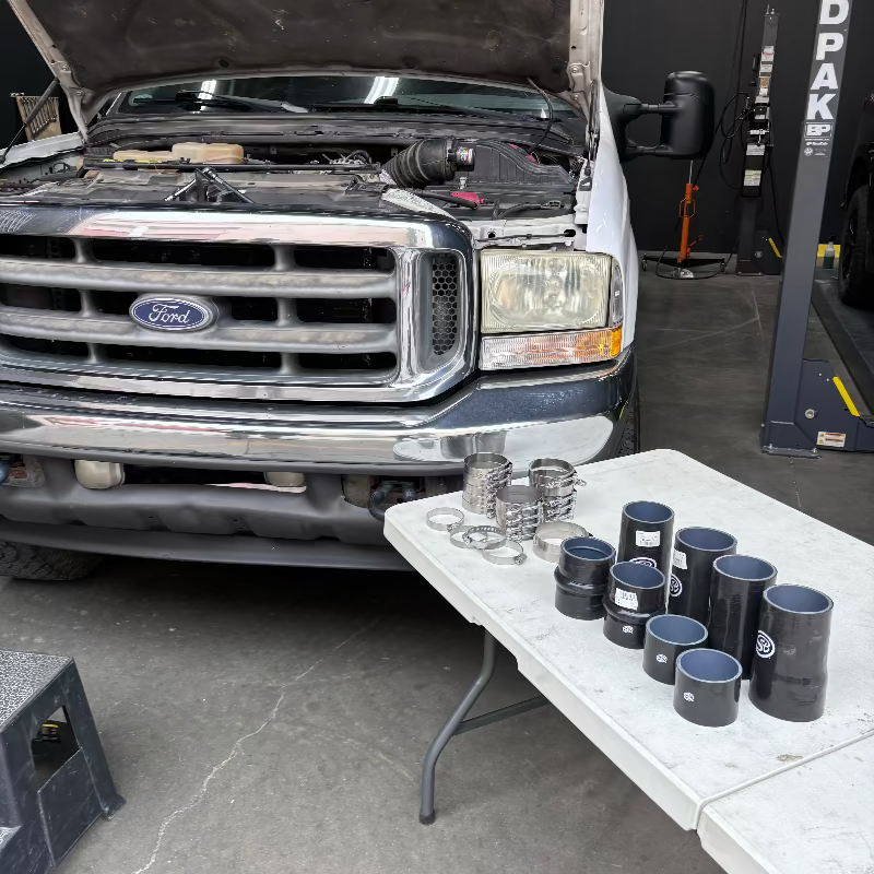 A set of SB Filters Hot and Cold Side Boot Kit for 1999.5-2003 Ford F250/F350, 7.3L Powerstroke, displayed on a table with a truck in the background.