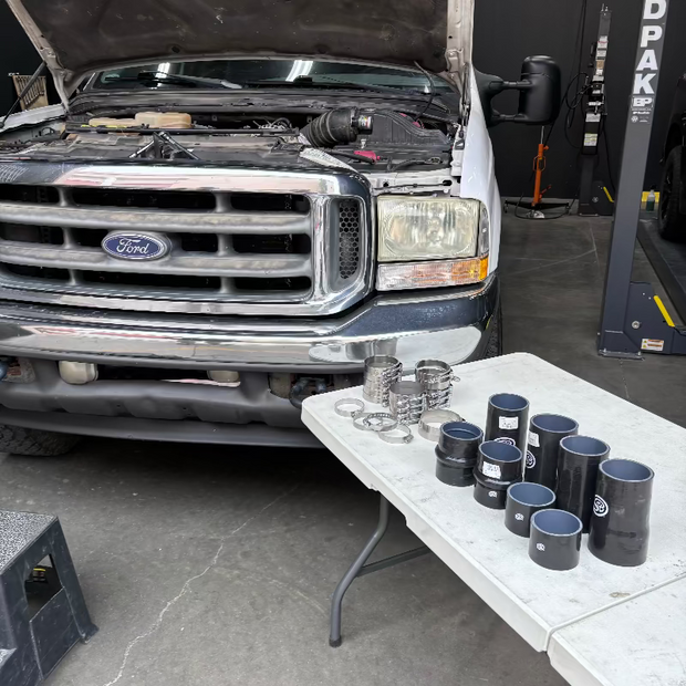 A set of SB Filters Hot and Cold Side Boot Kit for 1999.5-2003 Ford F250/F350, 7.3L Powerstroke, displayed on a table with a truck in the background.